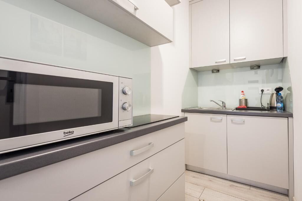 Een moderne keuken met witte kasten, een zwart aanrecht en een Beko magnetron.