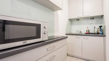 Een moderne keuken met witte kasten, een zwart aanrecht en een Beko magnetron.
