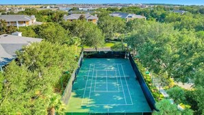 An aerial view of a tennis court surrounded by lush greenery and residential buildings. - Lakefront Condo w/ 6 Heated Pools | Near Disney! (Davenport)