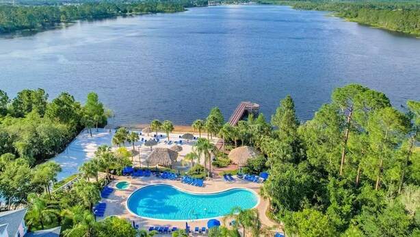 A resort with a large swimming pool surrounded by palm trees and lounge chairs, overlooking a large body of water. - Lakefront Condo w/ 6 Heated Pools | Near Disney! (Davenport)