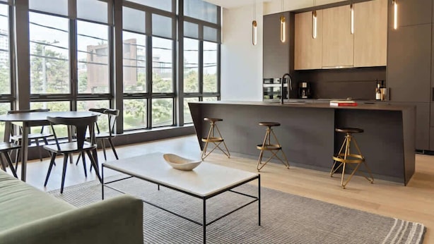 A modern kitchen with large windows, a dining area with a table and chairs, and a bar with stools.