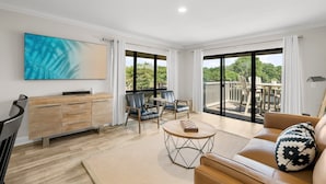 A spacious living room with a wooden cabinet, two leather chairs, a round coffee table, and a sofa with a patterned pillow. - Golf Cart ~ Golf Course & Lake Views (Miramar Beach)