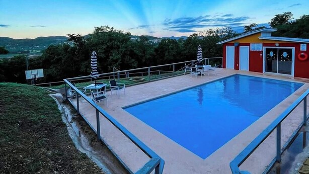Une piscine avec un bâtiment rouge en arrière-plan, entourée de verdure et sous un ciel dégagé.