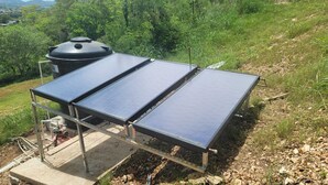 Une installation de panneaux solaires sur une pente, avec une structure métallique et un réservoir noir en arrière-plan.