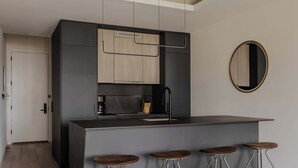 A modern kitchen with a dark countertop, wooden cabinets, and a black faucet. There are four stools with metal legs and wooden seats.