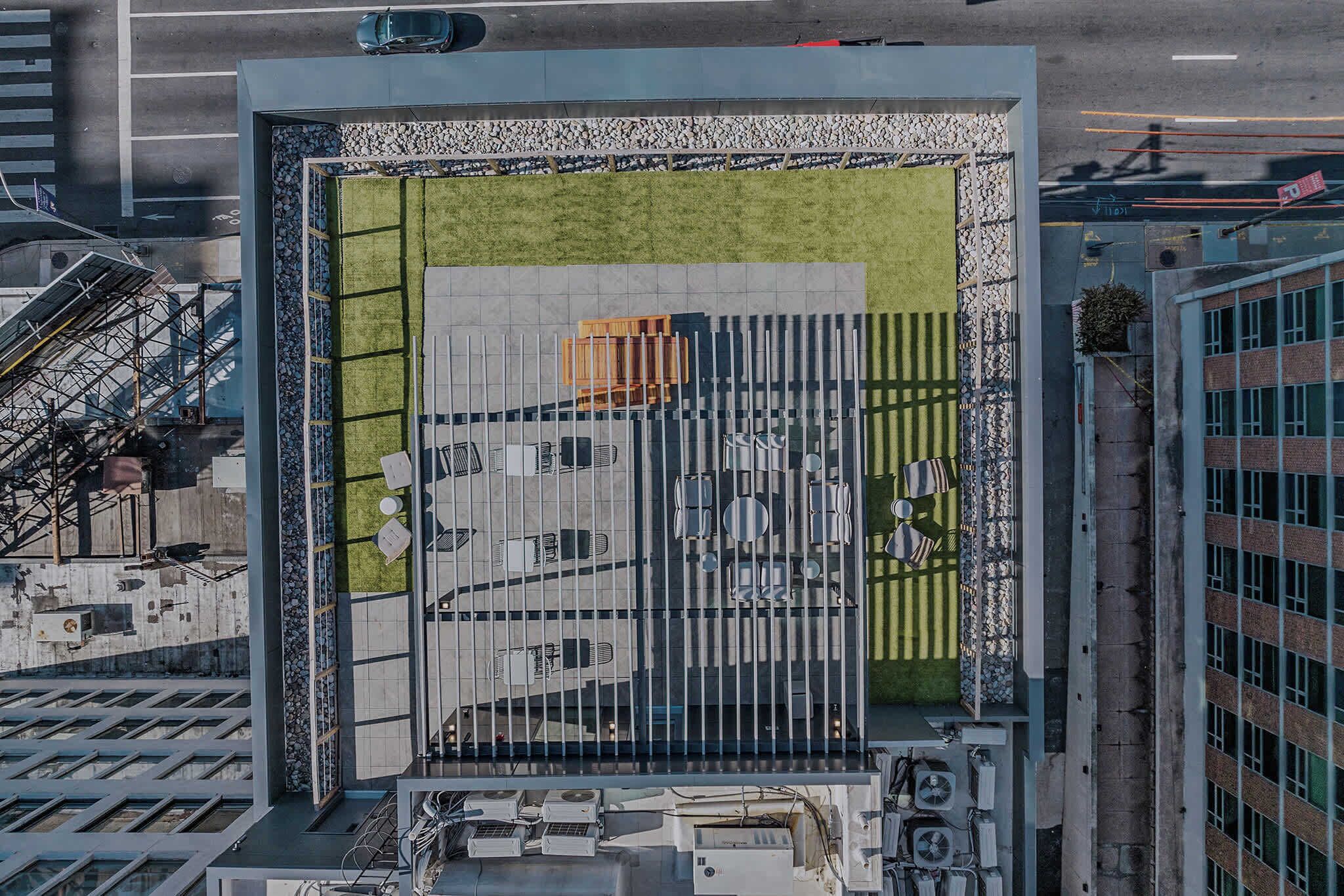 Un edificio moderno con terraza en la azotea que cuenta con césped, zona de estar y un amplio ventanal con persianas verticales.