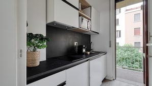 A modern kitchen with white cabinets, a black countertop, and a built-in oven. There is a potted plant on the counter and a window with a view of a building and greenery outside. - Delightful studios near Parco Tre Torri (Milan)