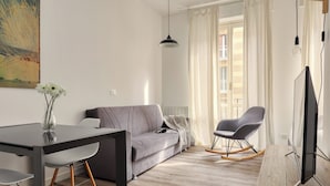 A modern living room with a grey sofa, a dining table with chairs, a rocking chair, and a flat-screen TV. - Delightful studios near Parco Tre Torri (Milan)