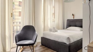A modern bedroom with a bed, a chair, and a window with curtains. - Delightful studios near Parco Tre Torri (Milan)