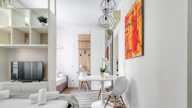 A modern hotel room with a bed, a TV, a dining area with a table and chairs, and a large window. - Delightful studios near Parco Tre Torri (Milan)