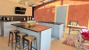 A modern kitchen with a central island, bar stools, a sink, and a dining area with a table and chairs. - Villa Oscar (Les Mesnuls)