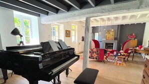 A spacious room with a grand piano, a bench, and a fireplace. - Villa Oscar (Les Mesnuls)