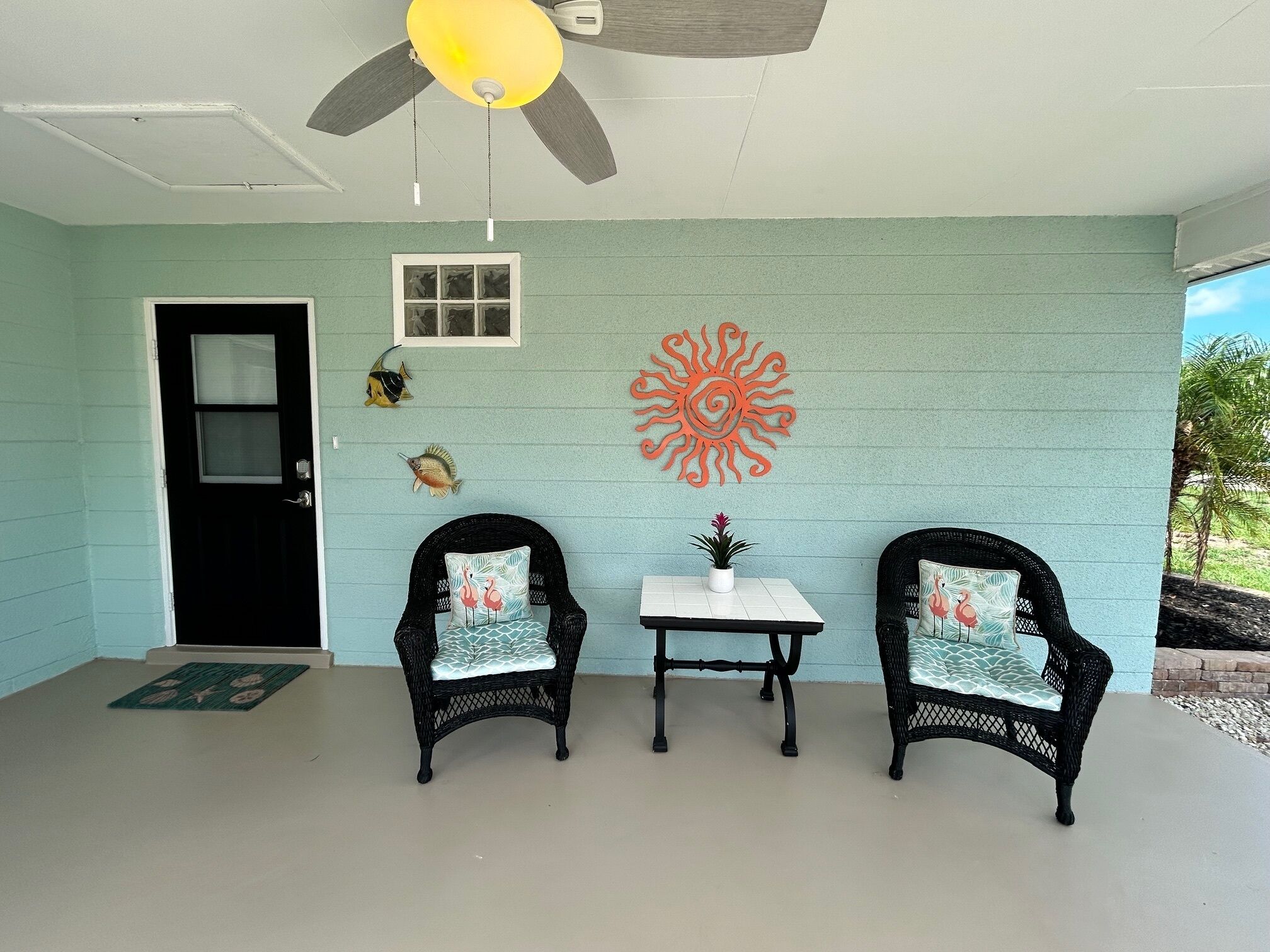 Une véranda avec deux fauteuils en osier, une petite table et des éléments décoratifs fixés au mur.