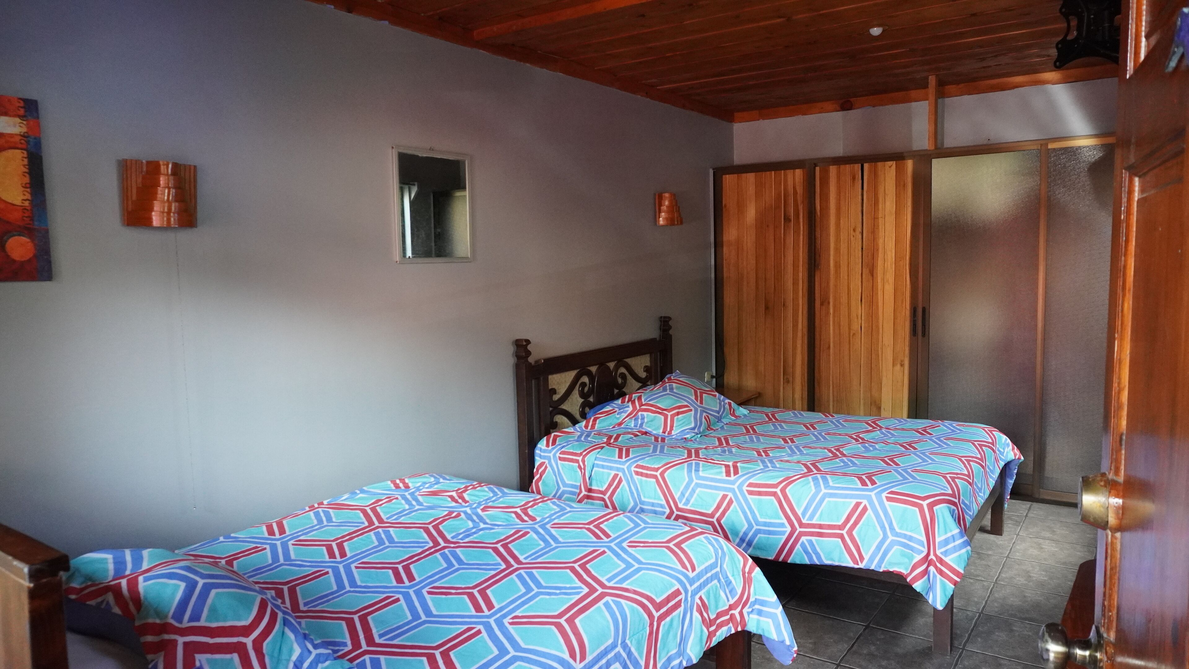 A room with two beds, wooden ceiling, and a door with a brass handle.