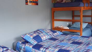 A room with two bunk beds, each with a blue plaid bedspread and pillows. There are wall-mounted lamps and a wooden ceiling.