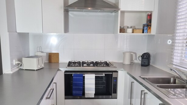 A modern kitchen with white cabinets, a built-in oven, a gas stove, and a dishwasher. - City View 3 Bedrooms & Work from Home Office, close to airport (Koongamia)