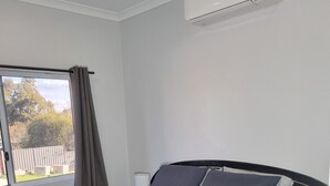 A neatly made bed with a dark blue bedspread and white towels, a bedside table with a lamp, and a window with curtains. - City View 3 Bedrooms & Work from Home Office, close to airport (Koongamia)