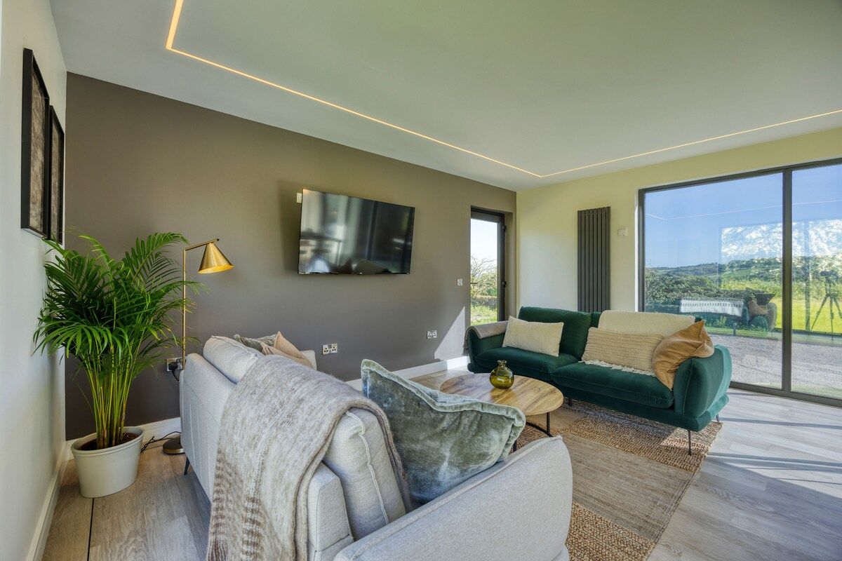 A modern living room with a sofa, a coffee table, a TV, and a large window offering a view.