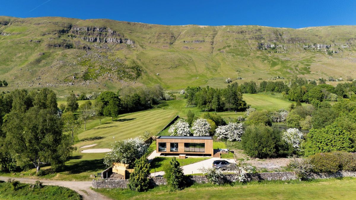 A modern house with a large window, surrounded by a well-maintained lawn and a golf course in the background.