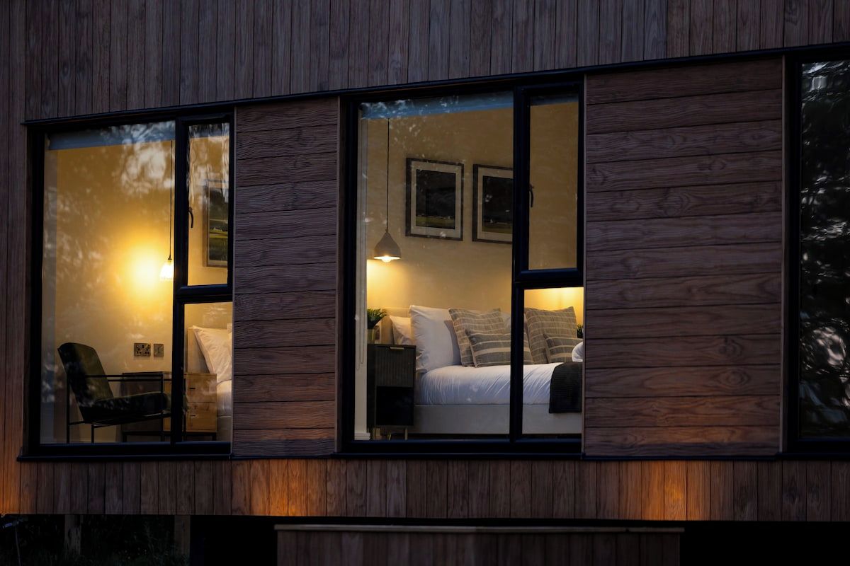 A modern interior with a bed, bedside table, lamp, and a chair.