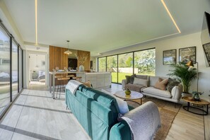 A spacious living area with a sofa, a coffee table, and a dining area with chairs. - Retreat to the Campsies (Lennoxtown)