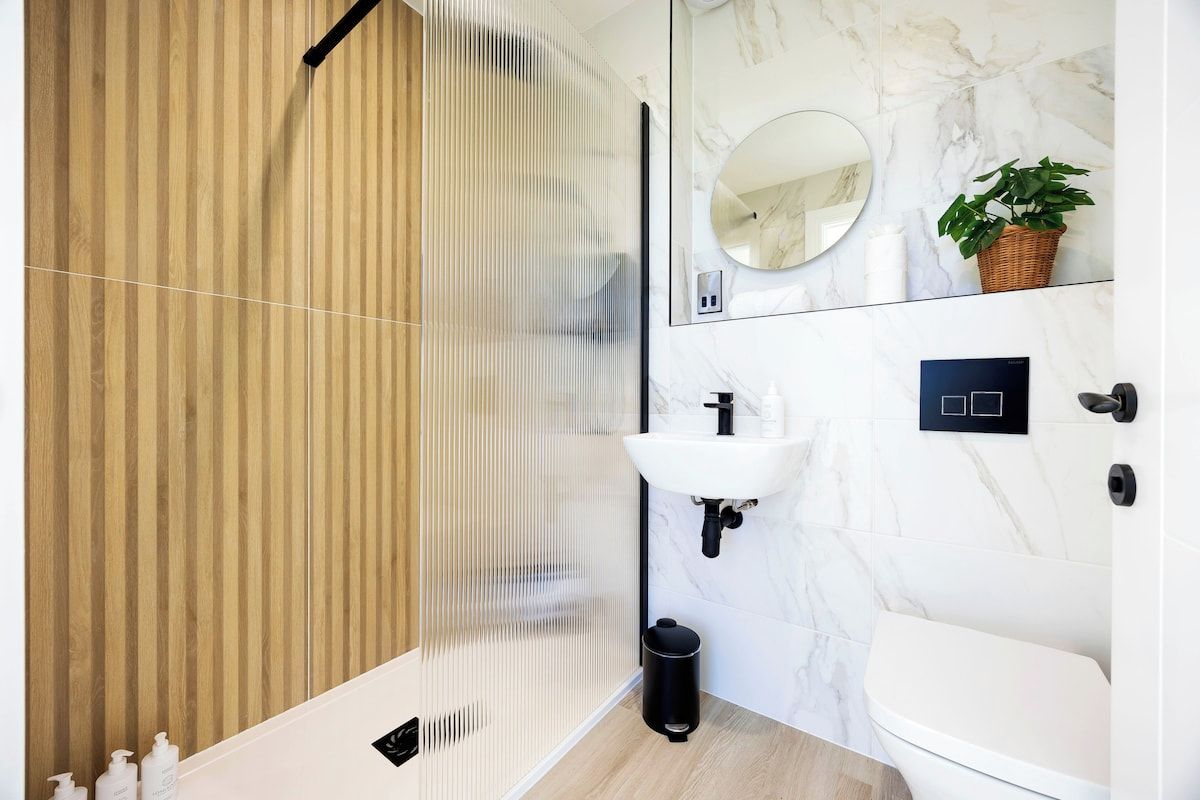 A modern bathroom with a wooden panel wall, a glass shower enclosure, a white sink, and a toilet.