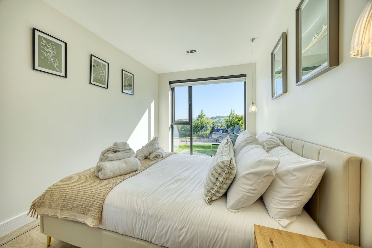 A bedroom with a bed, a large window, and a view of the outdoors.