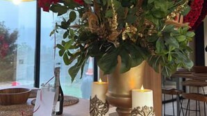 Et bord med en vase røde roser, to lys og en dekorativ guldfigur.