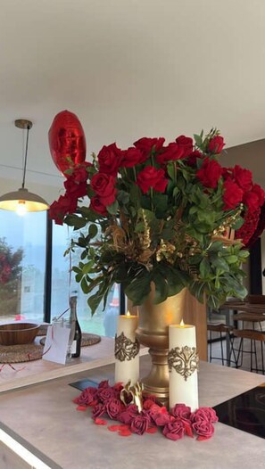 Una mesa con un florero de rosas rojas, dos velas y una figura decorativa dorada.