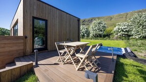 En moderne træbygning med terrasse, udendørs møbler og et spabad.