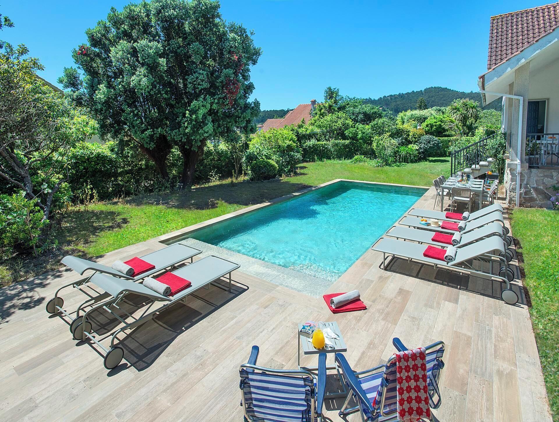 Una piscina rectangular amb gandules i una taula amb una beguda.