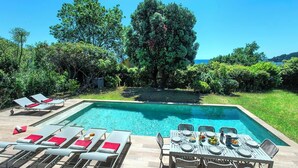 Une piscine rectangulaire, agrémentée de chaises longues et d’une table à manger installée pour les repas en plein air.
