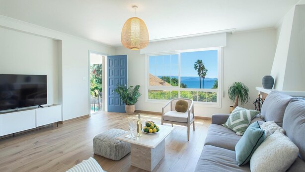 Un salon moderne doté d’un téléviseur à écran plat, d’un canapé, d’une table basse et offrant une vue sur la mer grâce à de grandes fenêtres.