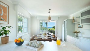 Une cuisine lumineuse avec un grand îlot central, des meubles blancs et une vue sur l’océan.