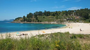 Une plage avec une eau d’un bleu limpide, un rivage sablonneux et, en arrière-plan, une colline boisée.