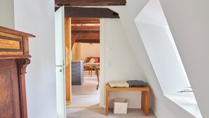 Une pièce avec un plafond en pente, un banc en bois, une petite table et un panier posé sur le sol.