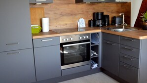 Une cuisine moderne avec des meubles gris, un plan de travail en bois, un four encastré, un évier et une machine à café.
