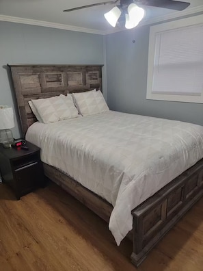 A bedroom with a wooden headboard, a white bedspread, a nightstand with a clock, and a ceiling fan.
