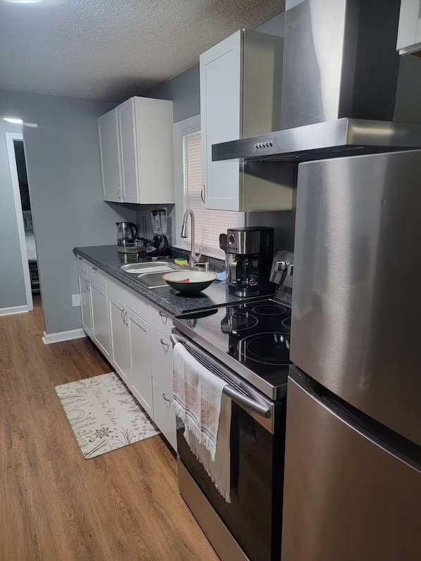 Uma cozinha moderna com eletrodomésticos de aço inoxidável, armários brancos e piso de madeira.