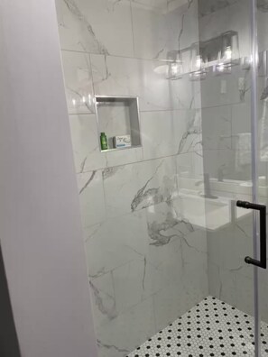 Ein modernes Duschbad mit Glastür, Marmorwänden und einem Boden in Hexagonoptik.