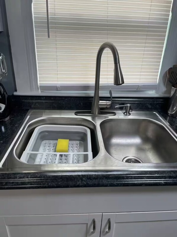 A stainless steel kitchen sink with a double basin, a yellow sponge, and a dish rack.