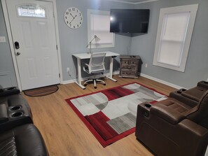 A living room with a desk, leather chairs, a TV, and a clock on the wall.