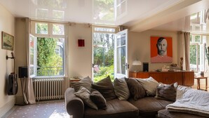 Una sala de estar acogedora con un sofá marrón, un radiador y una ventana con vistas a un jardín.