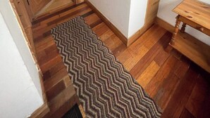 Un couloir doté d’un plancher en bois, d’un tapis à motifs en zigzag, d’une porte en bois et d’une petite table en bois.