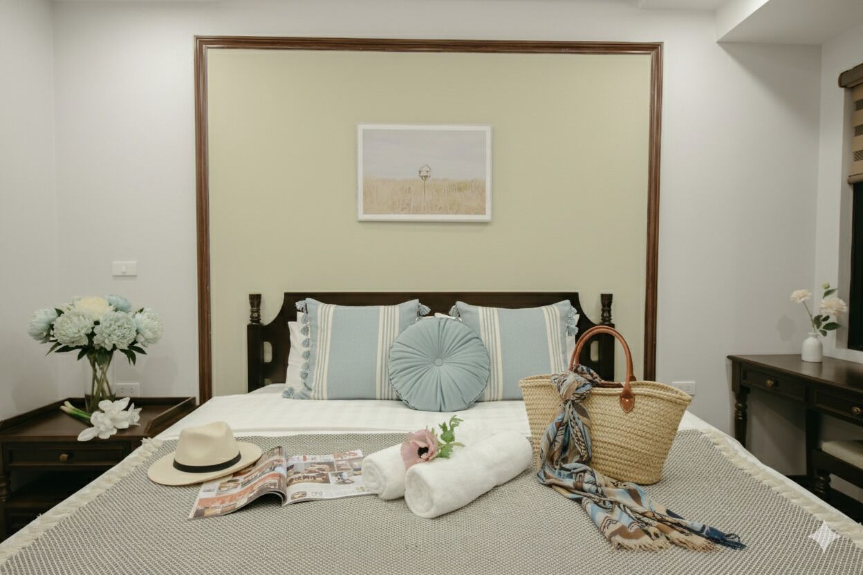 A neatly arranged bedroom with a bed, pillows, a bedside table with a vase of flowers, and a framed picture on the wall.