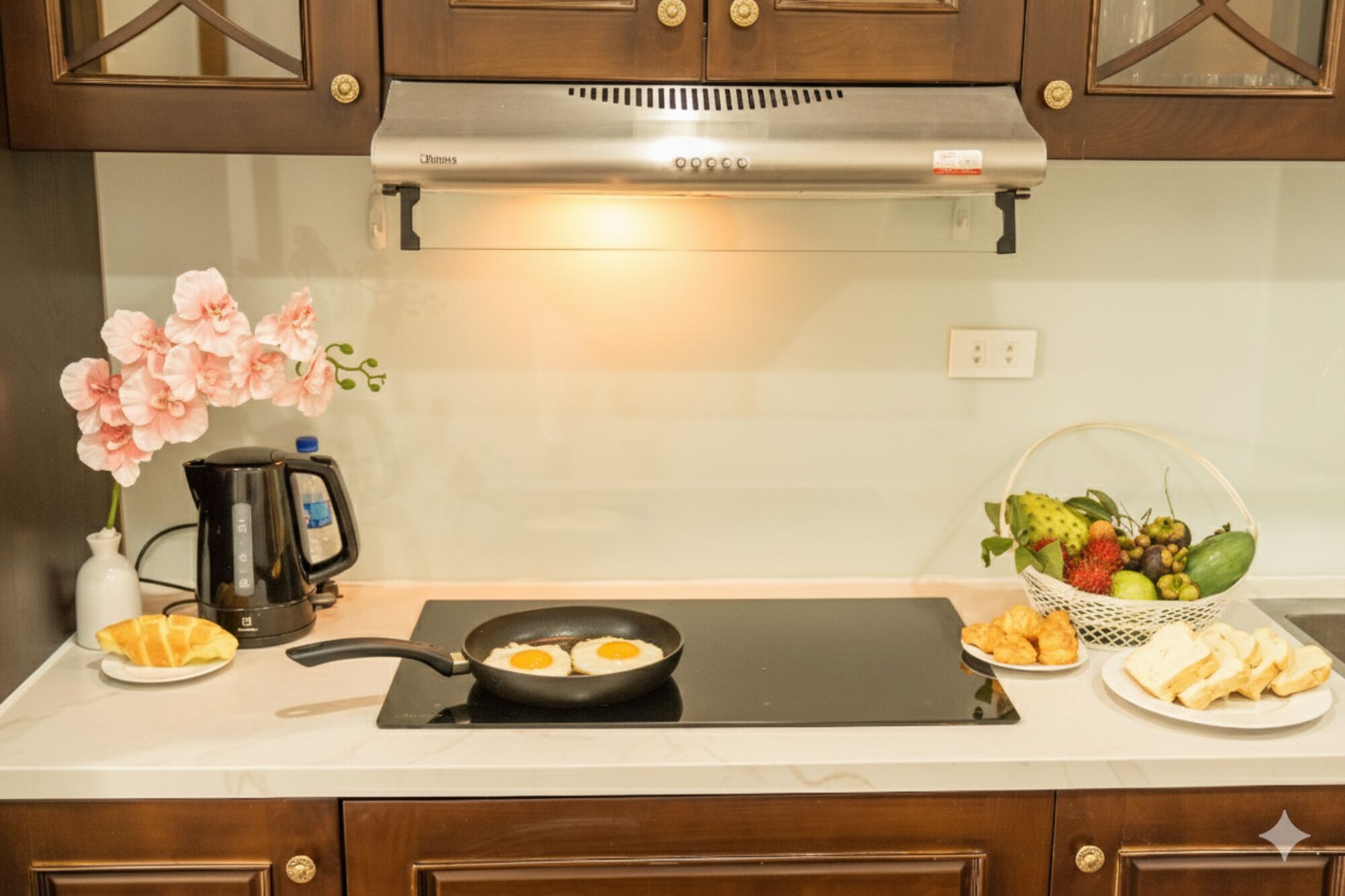 Une cuisine équipée d’une cuisinière, d’une machine à café, d’un panier de fruits et d’une assiette de croissants.