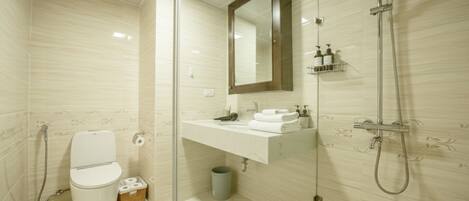 A modern bathroom with a glass shower enclosure, a toilet, a sink with a mirror, and a small trash bin.