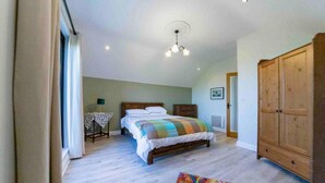 A bedroom with a bed, a wooden wardrobe, a table with a lamp, and a colorful rug. - Stylish Woodland Retreat With Balcony Views (Wingfield)