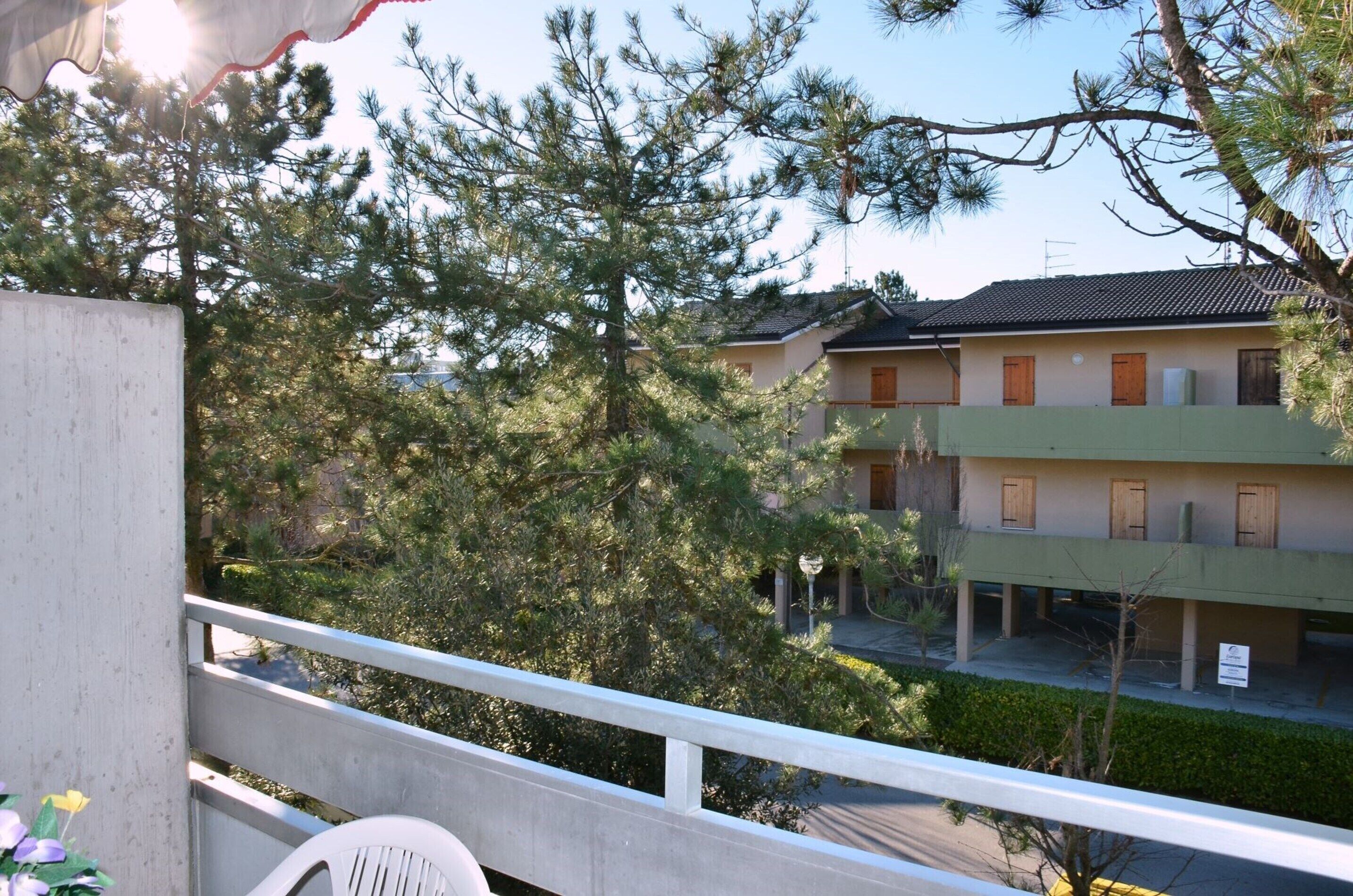 Ein Wohngebäude mit Balkon, umgeben von Bäumen und blauem Himmel.