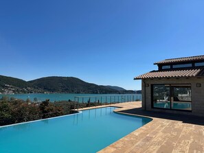 A swimming pool with a view of a lake and mountains, a building with large windows, and a tiled roof. - Smaragdine Blue Villa (Lefkada)